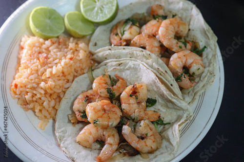 Shrimp tacos, with a red rice soup and some sliced lemons on the side on the plate.