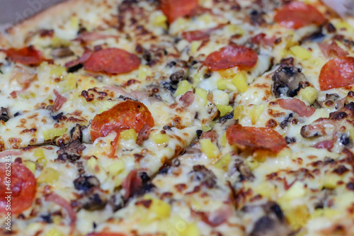 Close up of Pizza complete with cheese, salami, pineapple, mushrooms and condiments, weekend dinner, family.