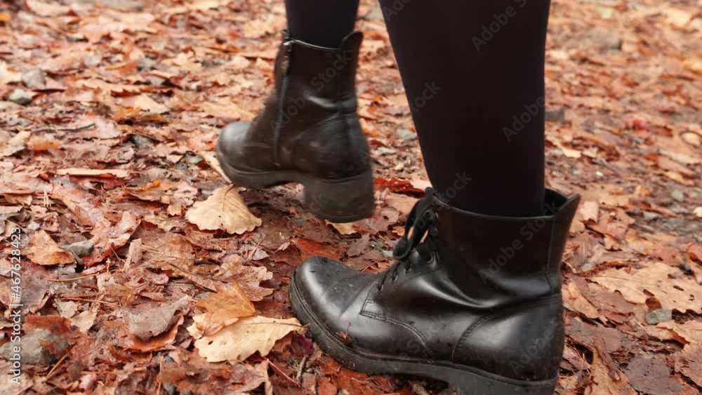 A beautiful girl is walking through the autumn forest. Close-up. A girl walks on fallen autumn leaves in black boots. A beautiful girl is walking through the autumn forest. Close-up. A girl walks on fallen autumn leaves in black boots.