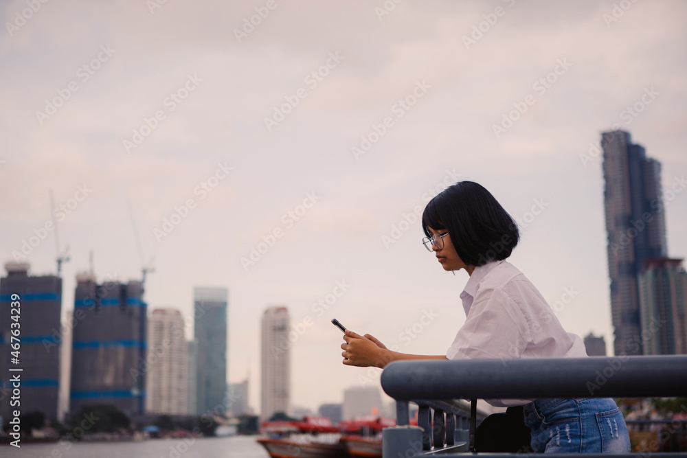 asian teenager reading message in mobile phone standing against city skyline asian teenager reading message in mobile phone standing against city skyline