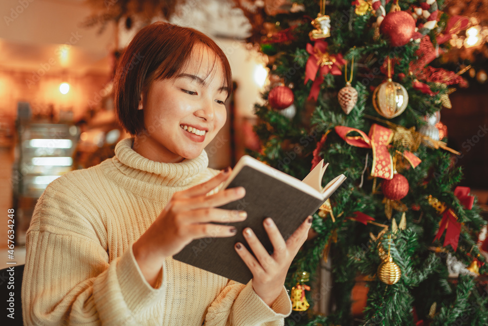 a young Woman in front of Christmas tree reading a book at home with x-mas decoration. a young Woman in front of Christmas tree reading a book at home with x-mas decoration.