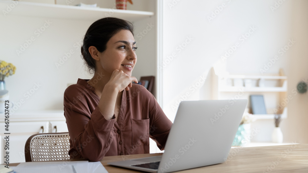 Attractive Indian woman sit at table with laptop thinking looks aside, brooding spend time alone at home, take break from study work on computer, search ideas, solve business lost in thoughts concept - obrazy, fototapety, plakaty 