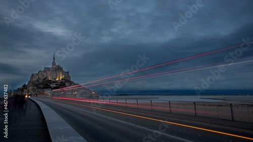 Vue du Mont Saint Michel à l'heure bleue avec, en avant plan, les lignes de phares d'un bus