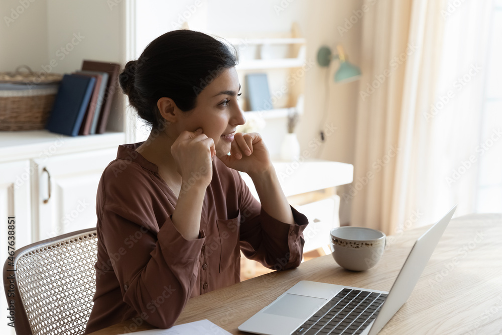 Distracted from computer work pensive young Indian female sit at table looking at distance, lost deep in thoughts, search new fresh creative ideas, ponder on task, spend weekend at home with laptop