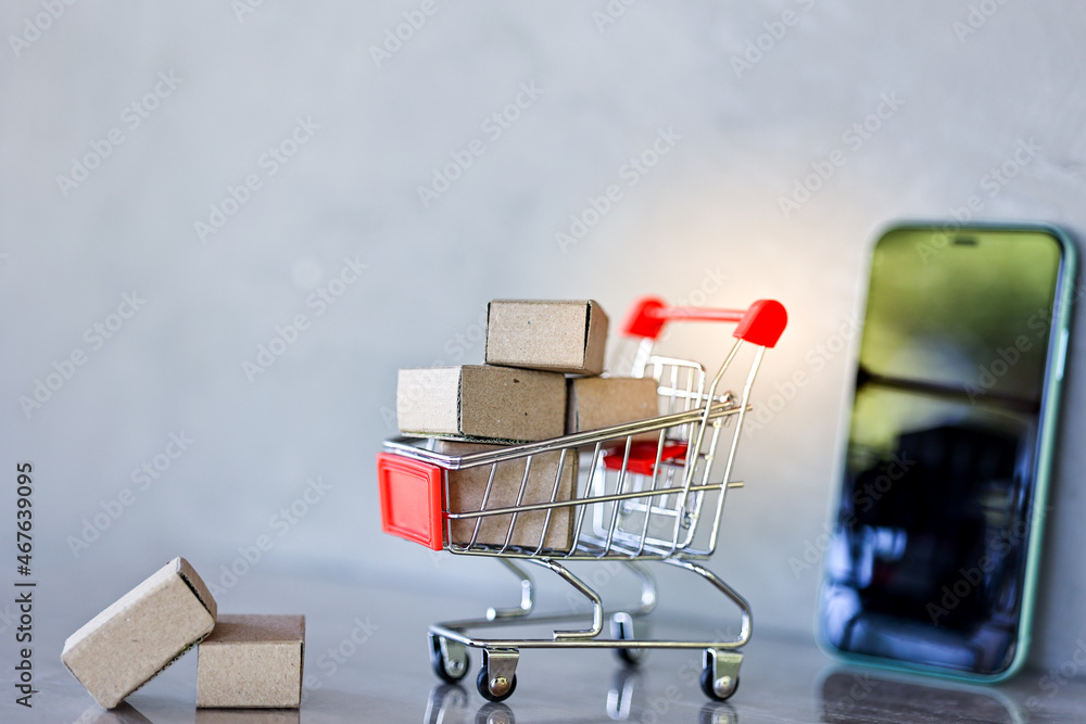 Shopping online and delivery concepts. Product package boxes in shopping cart with mobile phone on wooden table.