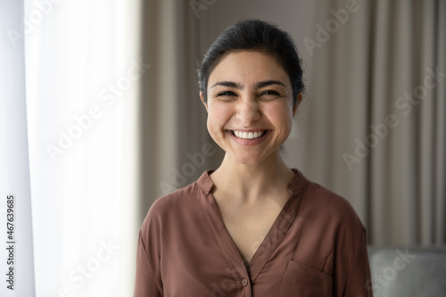 Head shot portrait cheerful cute Indian woman standing in living room looking at camera. Female having wide toothy smile advertise dental services clinic, candid emotions happy face expression concept