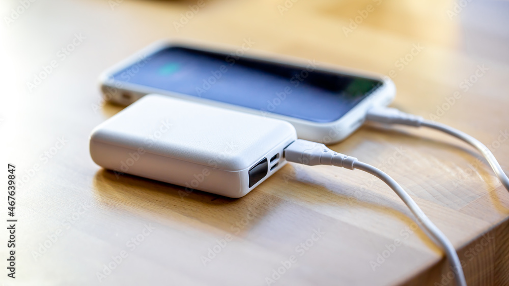 A smartphone is charged from a small white power bank. A smartphone is charged from a small white power bank.