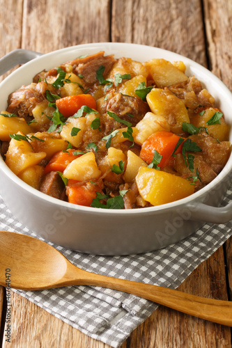 Traditional Scottish stovies consists of potatoes, meat, onions and carrots close up in the bowl on the table. Vertical