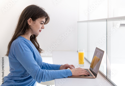 Attractive young woman with a glass of juice sits in front of a laptop.