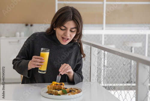 A woman is having breakfast with Belgian waffles and orange juice.