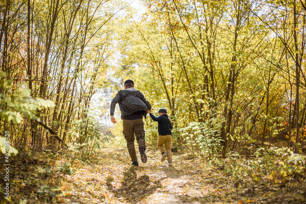 Fototapeta premium Father and son spend time in forest. Happy dad and child boy enjoying autumn time on vacation in a sunny park. Kids love parents affection and tenderness, lovely family.