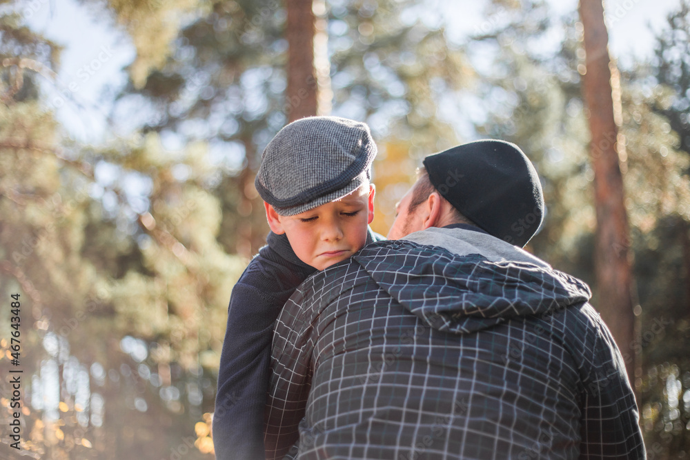 Father`s day. Sad son hugging dad on the forest background with copy space. Concept of father-son relationship Father`s day. Sad son hugging dad on the forest background with copy space. Concept of father-son relationship