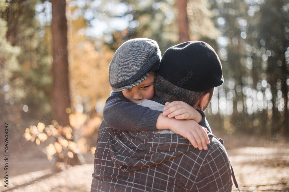 Father`s day. Sad son hugging dad on the forest background with copy space. Concept of father-son relationship Father`s day. Sad son hugging dad on the forest background with copy space. Concept of father-son relationship