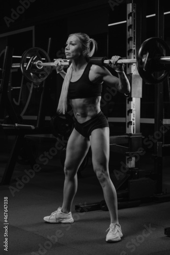 A fit woman is squatting with a barbell near the squat rack in a gym.