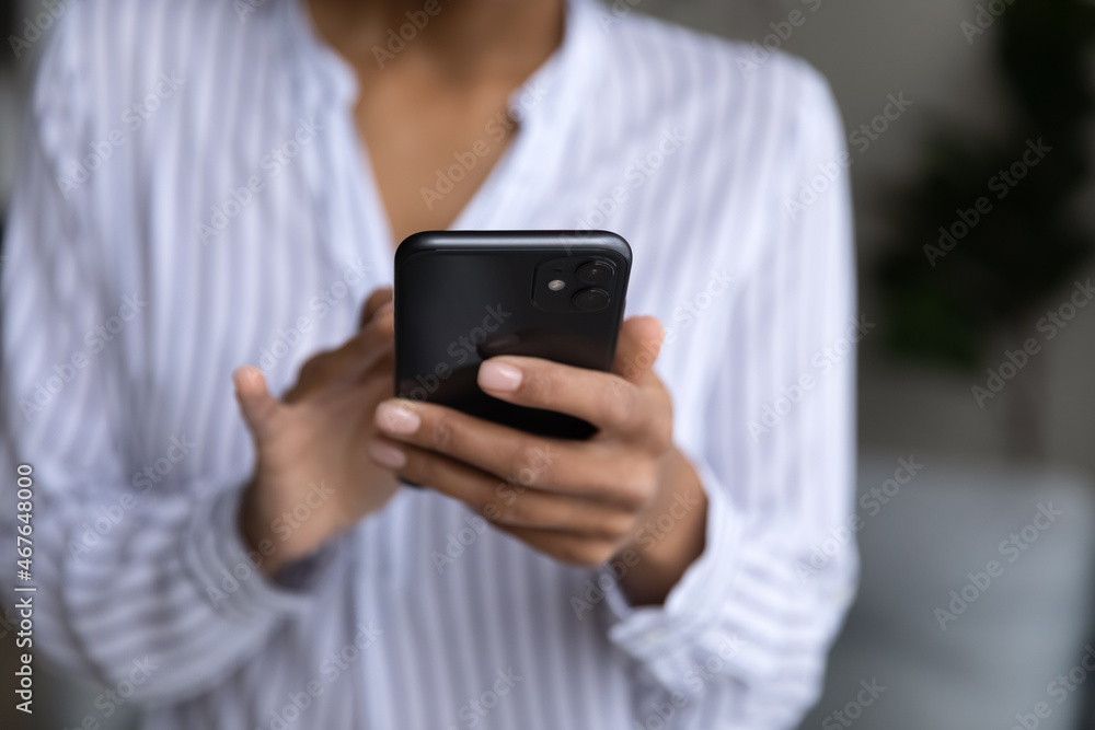 Cropped close up of African American woman holding modern smartphone in hands, typing on screen, writing message in social network, chatting or shopping online, browsing mobile device apps Cropped close up of African American woman holding modern smartphone in hands, typing on screen, writing message in social network, chatting or shopping online, browsing mobile device apps