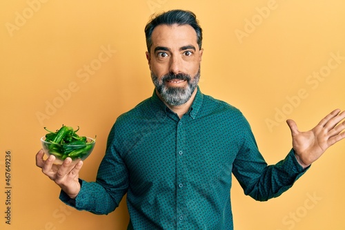 Middle age man with beard and grey hair holding green apples celebrating achievement with happy smile and winner expression with raised hand