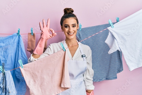Beautiful brunette young woman washing clothes at clothesline smiling positive doing ok sign with hand and fingers. successful expression.