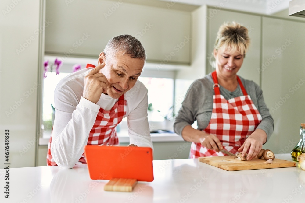 Senior caucasian couple smiling happy looking recipe on touchpad and cooking at the kitchen. Senior caucasian couple smiling happy looking recipe on touchpad and cooking at the kitchen.