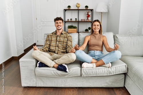 Young hispanic couple smiling happy doig yoga exercise sitting on the sofa at home. photo