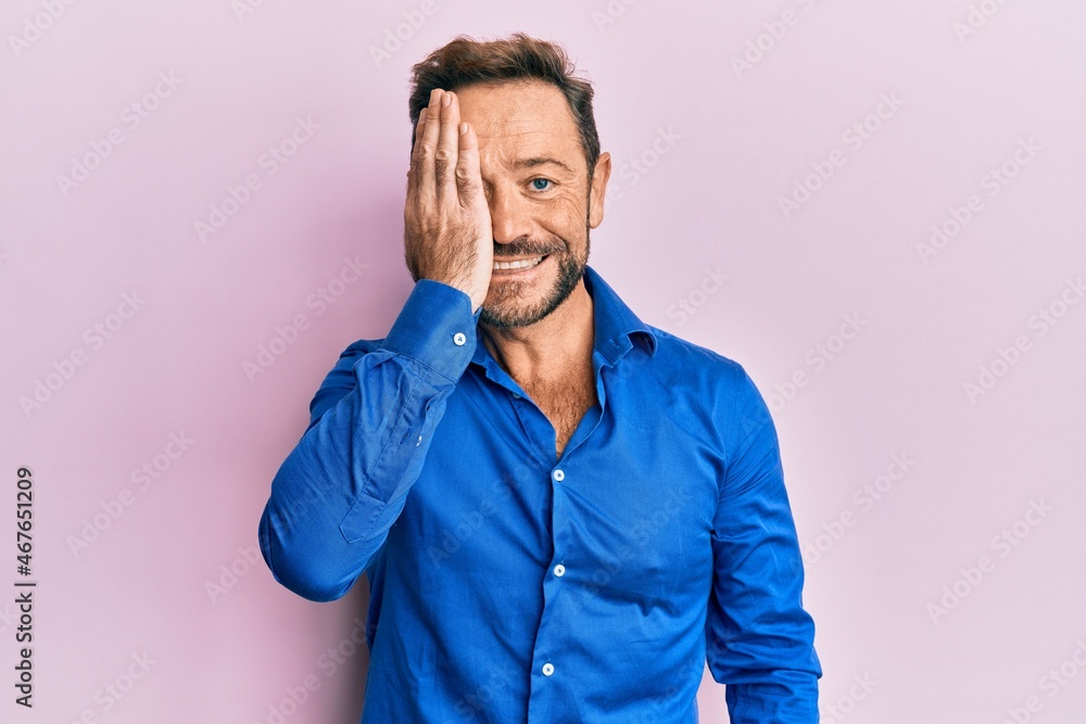 Middle age man wearing casual clothes covering one eye with hand, confident smile on face and surprise emotion.
