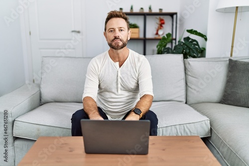 Middle age man using laptop at home relaxed with serious expression on face. simple and natural looking at the camera.