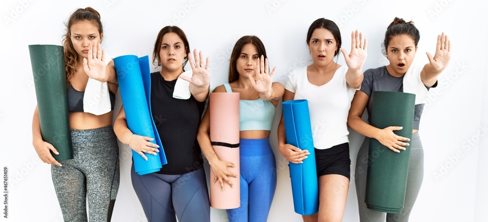 Group of women holding yoga mat standing over isolated background doing stop gesture with hands palms, angry and frustration expression Group of women holding yoga mat standing over isolated background doing stop gesture with hands palms, angry and frustration expression