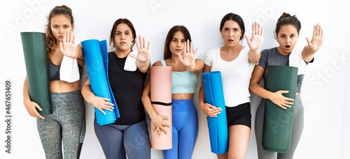 Group of women holding yoga mat standing over isolated background doing stop gesture with hands palms, angry and frustration expression