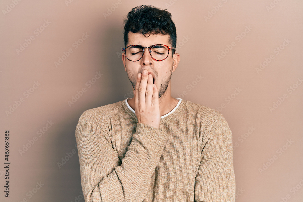 Young hispanic man wearing casual clothes and glasses bored yawning tired covering mouth with hand. restless and sleepiness. Young hispanic man wearing casual clothes and glasses bored yawning tired covering mouth with hand. restless and sleepiness.