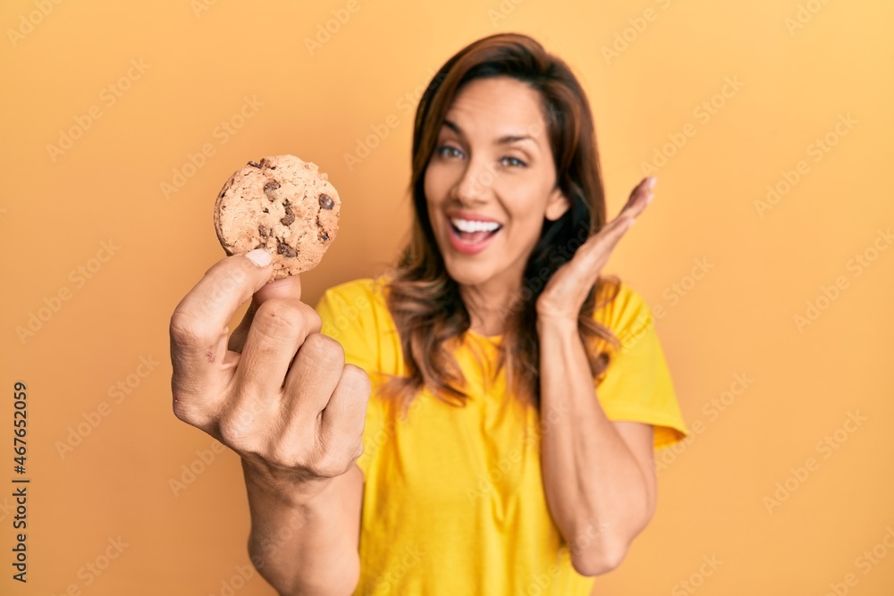 Young latin woman holding cookie celebrating achievement with happy smile and winner expression with raised hand Young latin woman holding cookie celebrating achievement with happy smile and winner expression with raised hand