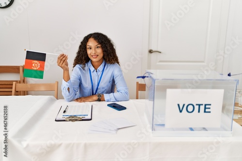 Young latin woman smiling confident holding afghanistan flag working at electoral college