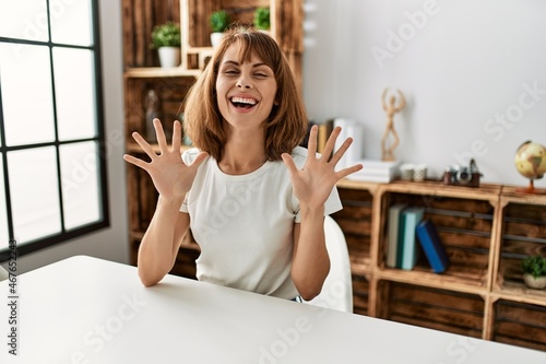 Young caucasian girl wearing casual clothes sitting on the table at home showing and pointing up with fingers number ten while smiling confident and happy.