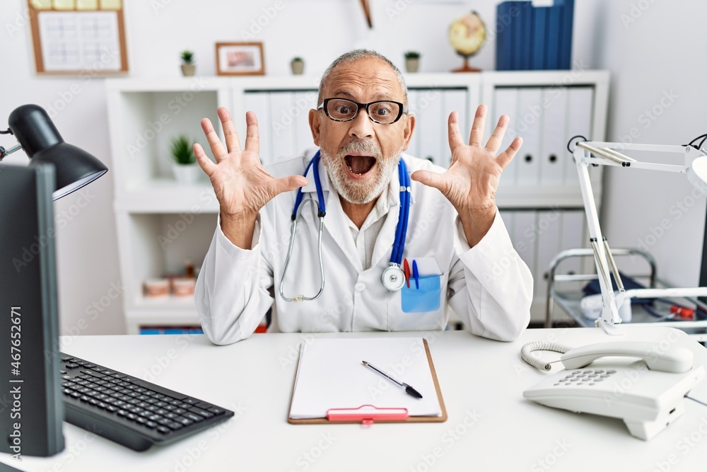Mature doctor man at the clinic celebrating crazy and amazed for success with arms raised and open eyes screaming excited. winner concept Mature doctor man at the clinic celebrating crazy and amazed for success with arms raised and open eyes screaming excited. winner concept