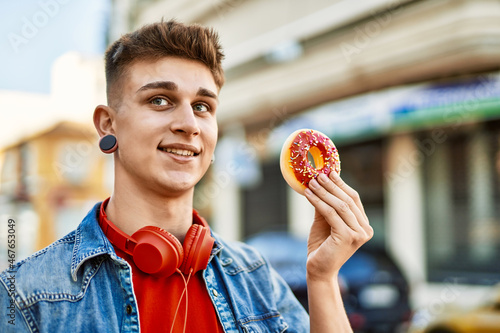 Young caucasian guy smiling holding doughnut at the city