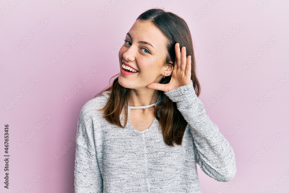 Young brunette woman wearing casual sweater smiling with hand over ear listening and hearing to rumor or gossip. deafness concept. Young brunette woman wearing casual sweater smiling with hand over ear listening and hearing to rumor or gossip. deafness concept.