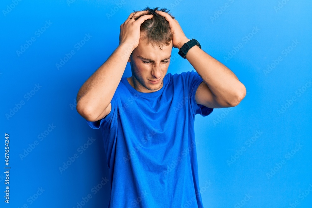 Young caucasian man wearing casual blue t shirt suffering from headache desperate and stressed because pain and migraine. hands on head. Young caucasian man wearing casual blue t shirt suffering from headache desperate and stressed because pain and migraine. hands on head.