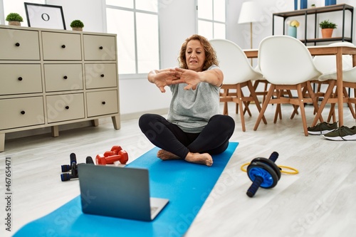 Middle age caucasian woman smiling confident using laptop stretching at home
