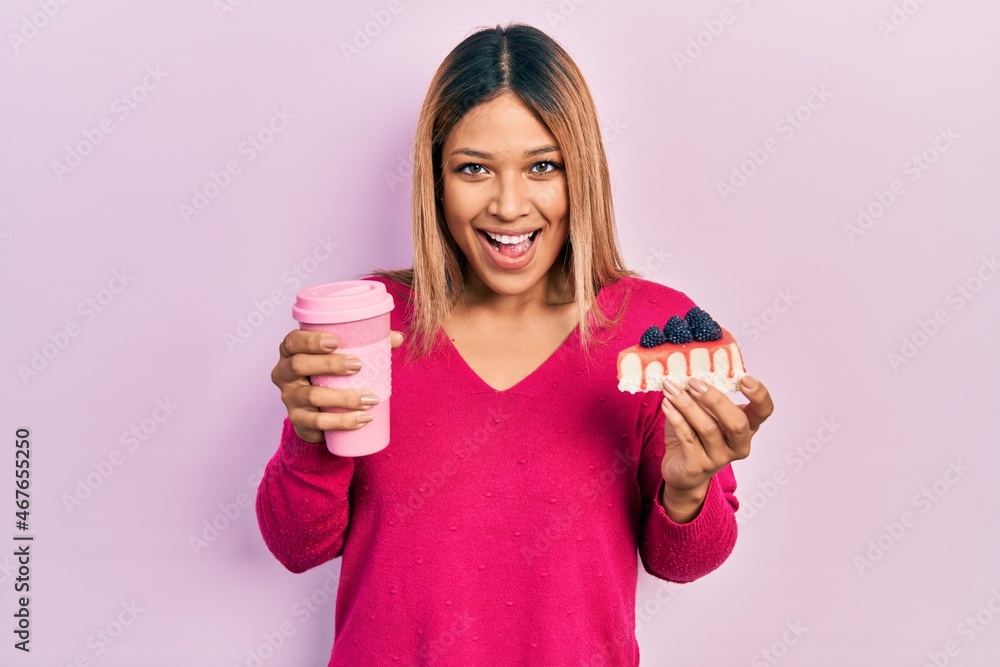 Beautiful hispanic woman holding takeaway cup of coffee and cheesecake smiling and laughing hard out loud because funny crazy joke. Beautiful hispanic woman holding takeaway cup of coffee and cheesecake smiling and laughing hard out loud because funny crazy joke.