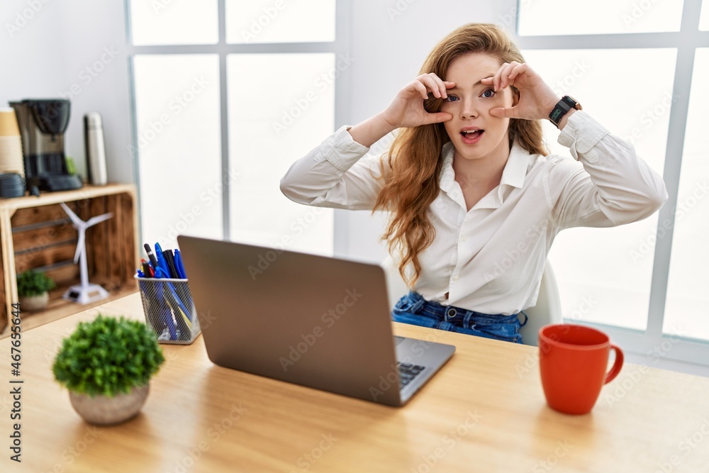 Young caucasian woman working at the office using computer laptop trying to open eyes with fingers, sleepy and tired for morning fatigue