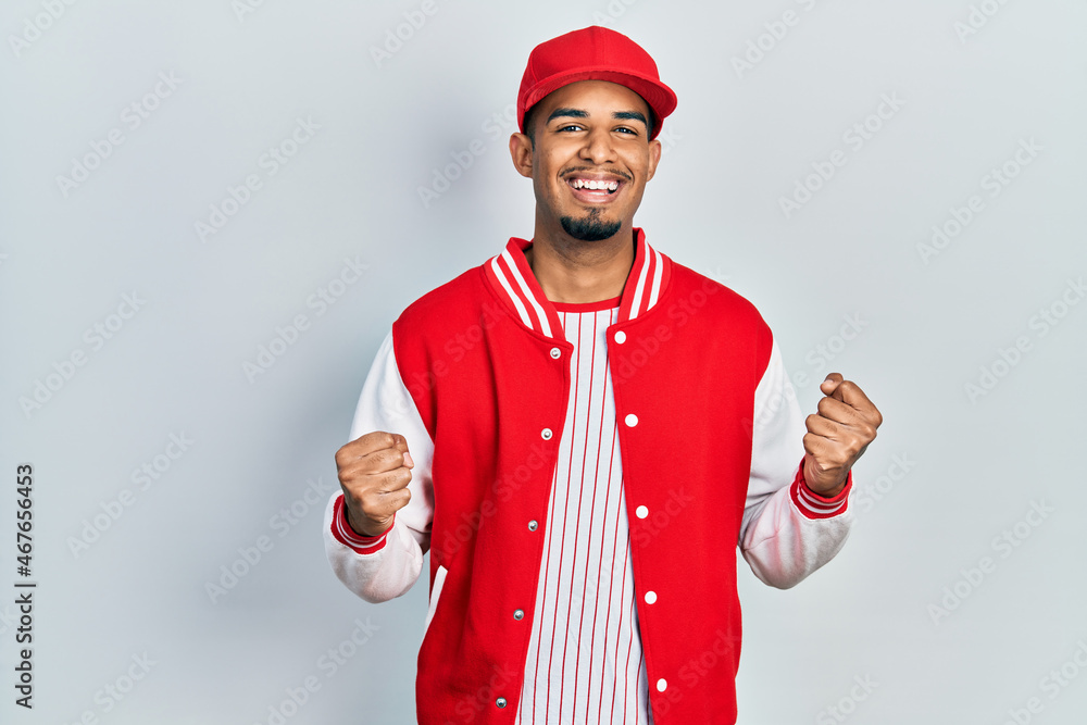 Young african american man wearing baseball uniform celebrating surprised and amazed for success with arms raised and open eyes. winner concept. Young african american man wearing baseball uniform celebrating surprised and amazed for success with arms raised and open eyes. winner concept.