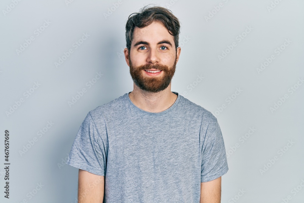 Caucasian man with beard wearing casual grey t shirt with a happy and cool smile on face. lucky person. Caucasian man with beard wearing casual grey t shirt with a happy and cool smile on face. lucky person.