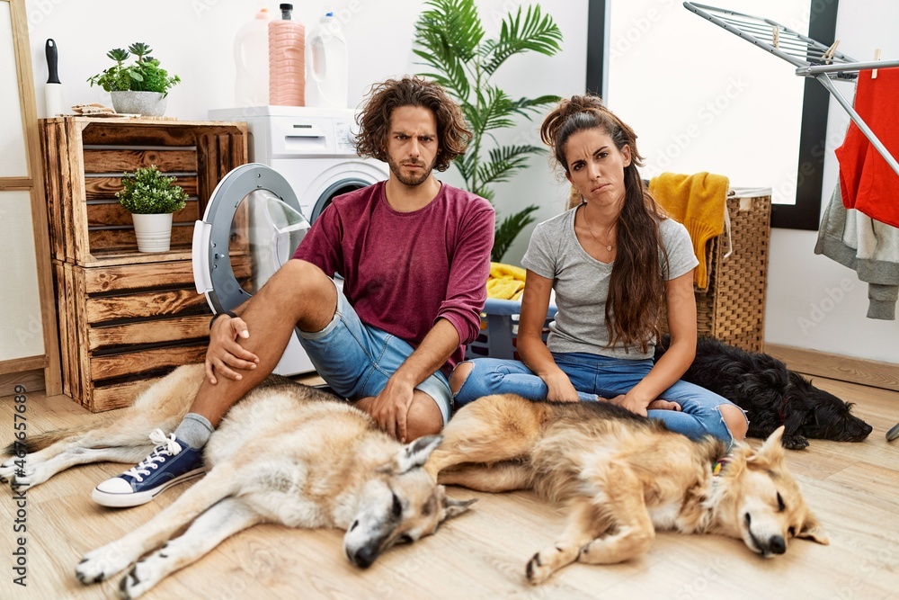 Obraz premium Young hispanic couple doing laundry with dogs skeptic and nervous, frowning upset because of problem. negative person.