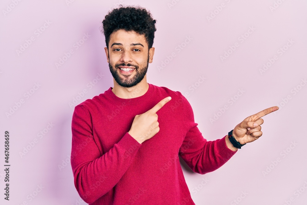 Young arab man with beard wearing casual pink sweater smiling and looking at the camera pointing with two hands and fingers to the side. Young arab man with beard wearing casual pink sweater smiling and looking at the camera pointing with two hands and fingers to the side.