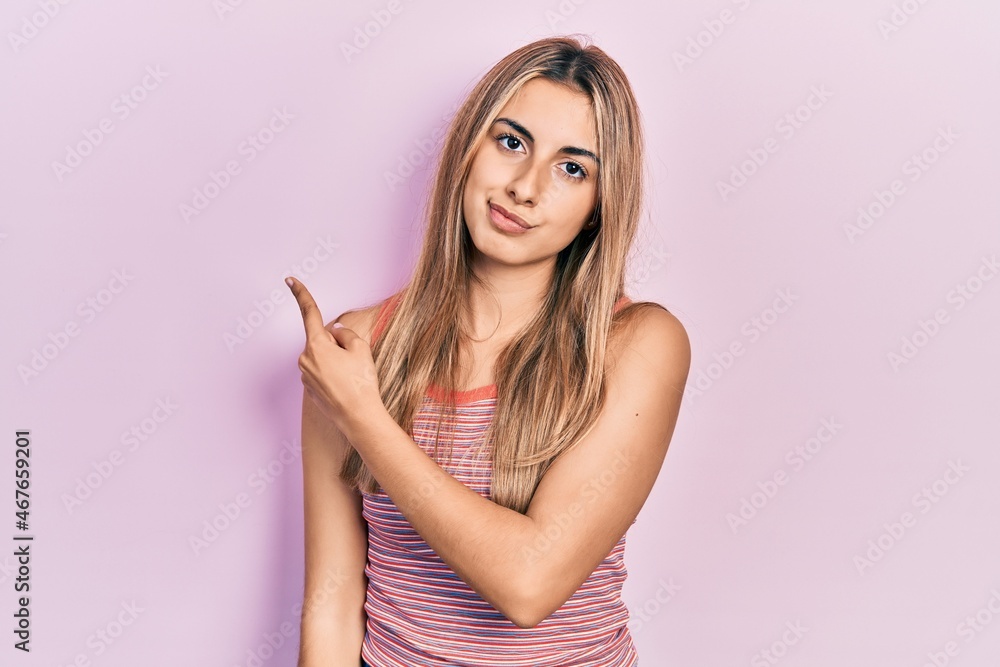 Beautiful hispanic woman wearing casual summer t shirt pointing with hand finger to the side showing advertisement, serious and calm face Beautiful hispanic woman wearing casual summer t shirt pointing with hand finger to the side showing advertisement, serious and calm face