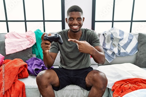 Young african american man playing video game sitting on the sofa smiling happy pointing with hand and finger