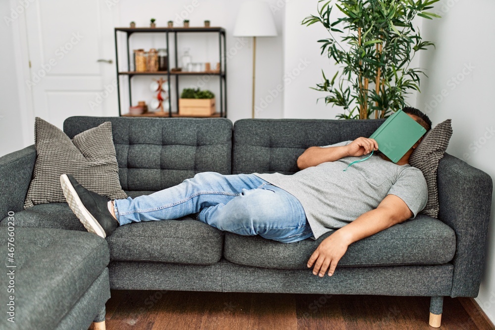 Young hispanic man sleeping with book on face lying on the sofa at home. Young hispanic man sleeping with book on face lying on the sofa at home.