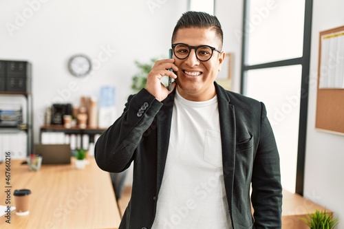 Young latin businessman smiling happy talking on the smartphone working at the office.