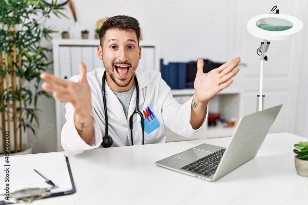 Young doctor working at the clinic using computer laptop celebrating crazy and amazed for success with arms raised and open eyes screaming excited. winner concept Young doctor working at the clinic using computer laptop celebrating crazy and amazed for success with arms raised and open eyes screaming excited. winner concept
