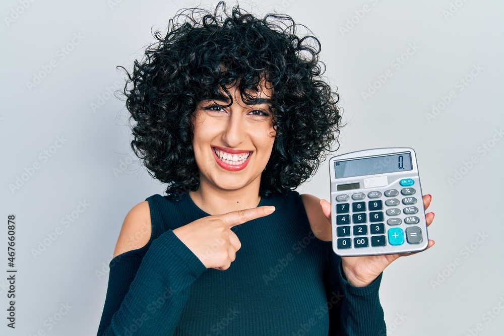Young middle east woman showing calculator device smiling happy pointing with hand and finger Young middle east woman showing calculator device smiling happy pointing with hand and finger