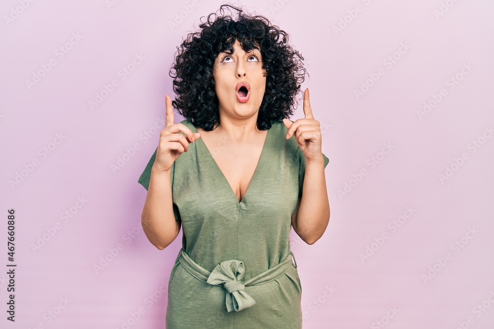 Young middle east woman wearing casual clothes amazed and surprised looking up and pointing with fingers and raised arms.
