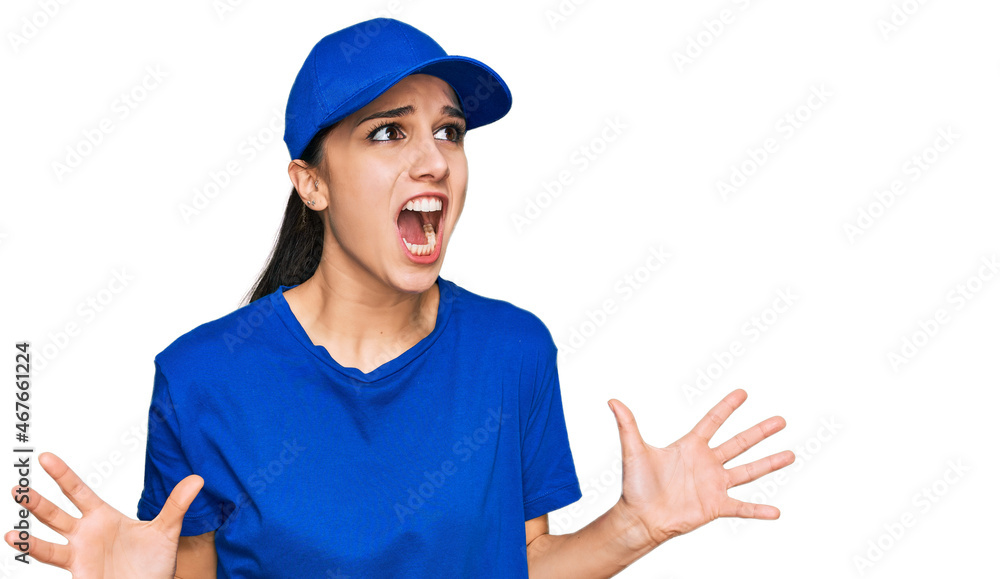 Young hispanic girl wearing delivery courier uniform crazy and mad shouting and yelling with aggressive expression and arms raised. frustration concept. Young hispanic girl wearing delivery courier uniform crazy and mad shouting and yelling with aggressive expression and arms raised. frustration concept.